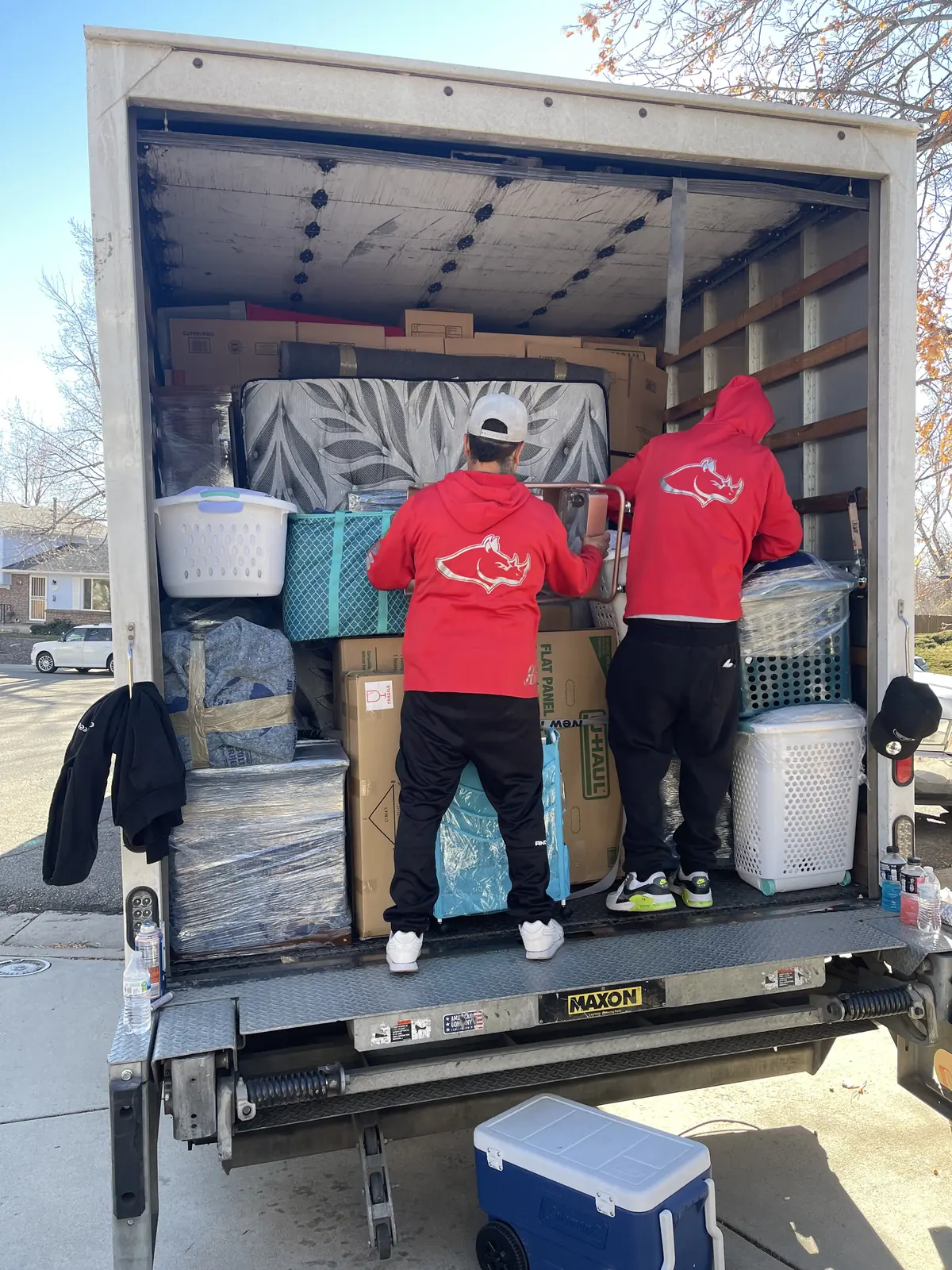 Two Rhino Brothers movers standing at the open rear of a loaded moving truck