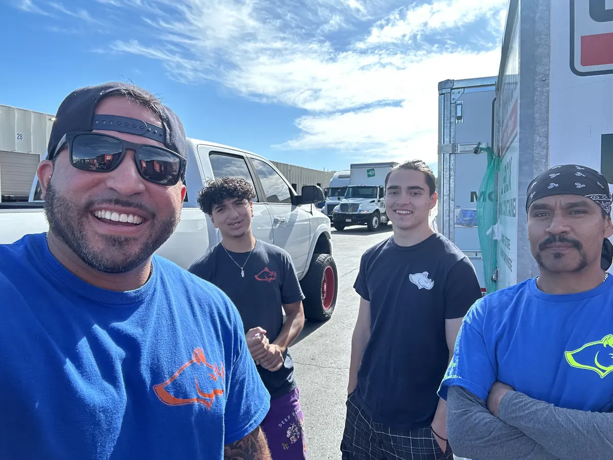Four Rhino Brothers crew members standing beside moving trucks