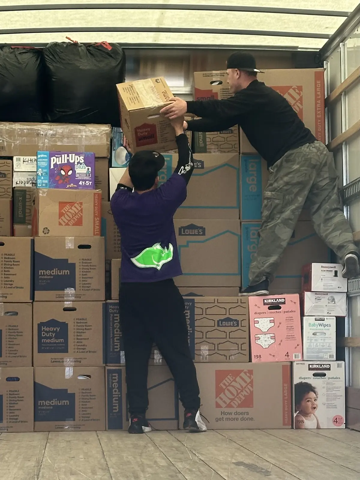 Two movers passing a cardboard box inside a truck stacked with moving boxes