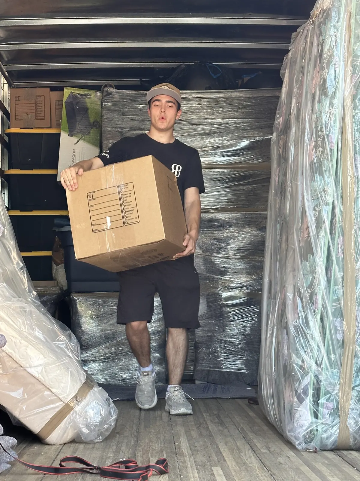 Mover holding a cardboard box inside a truck beside padded furniture