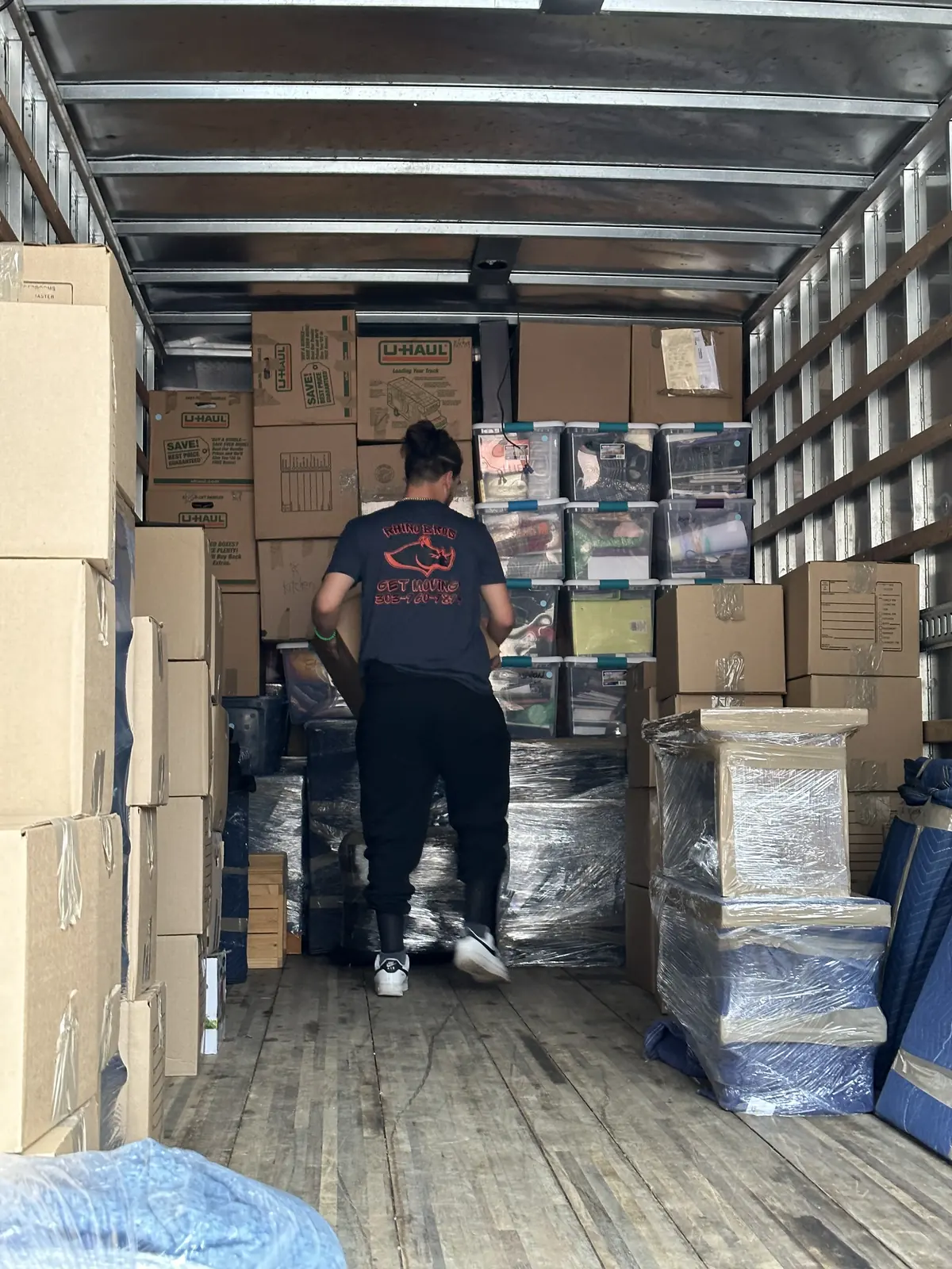 Mover standing inside a truck loaded with boxes and wrapped furniture