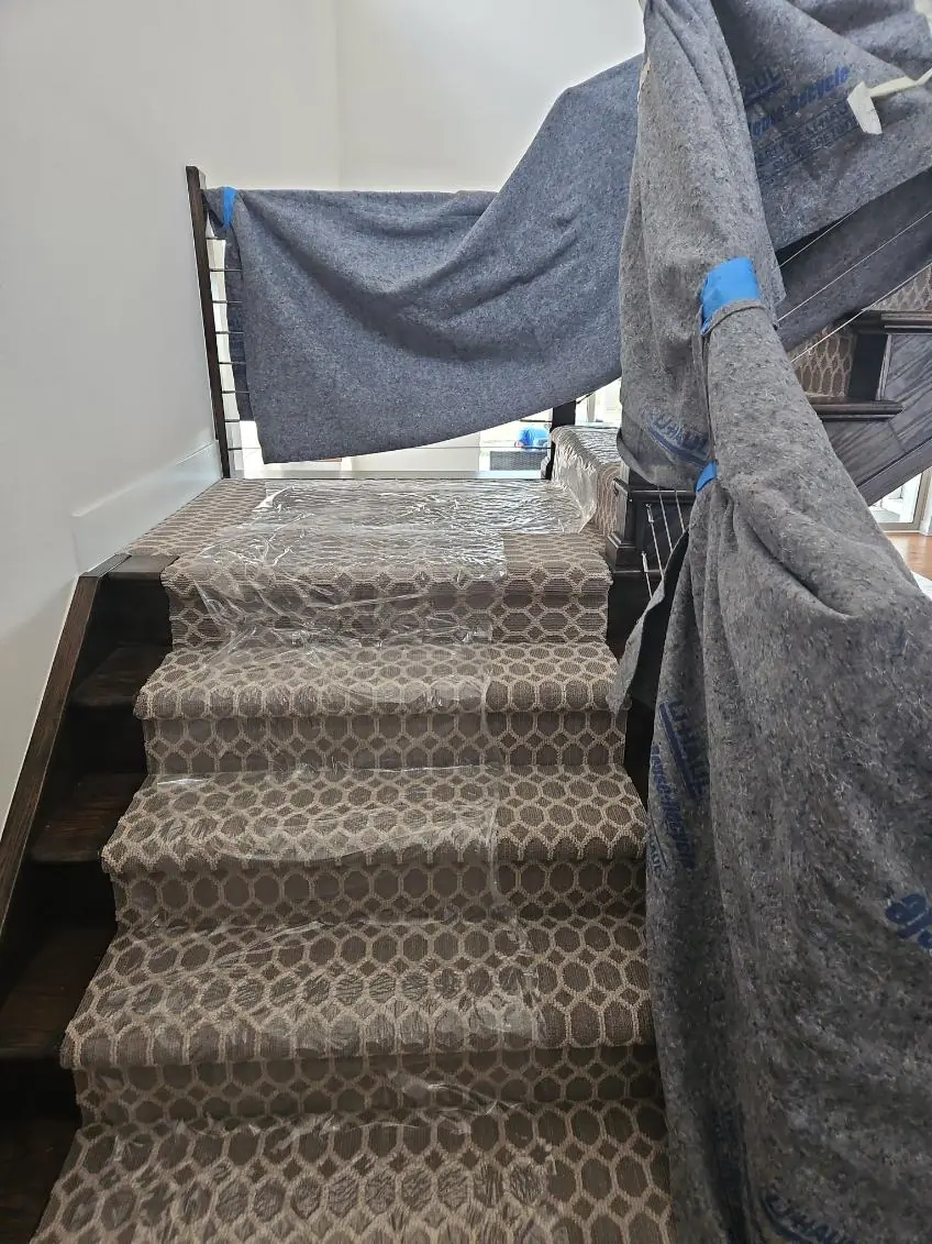 Carpeted stairs with moving blankets over the railings and surrounding walls
