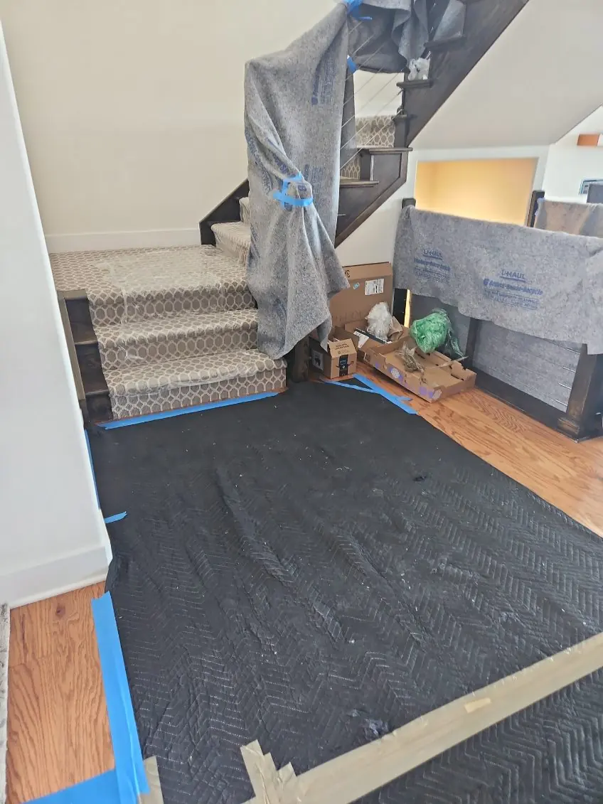 Entryway with a black floor runner and moving blankets around the stairs