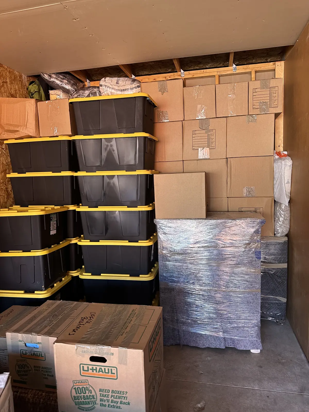 Furniture covered in dark moving blankets and stretch wrap beside stacked boxes