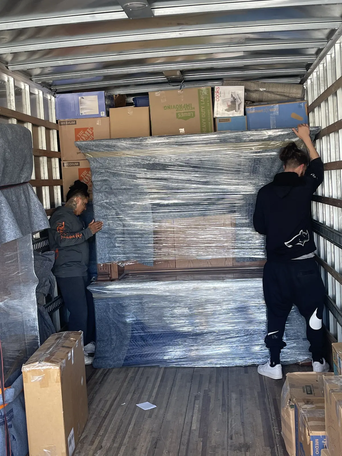 Two movers inside a truck with large furniture pieces covered in stretch wrap