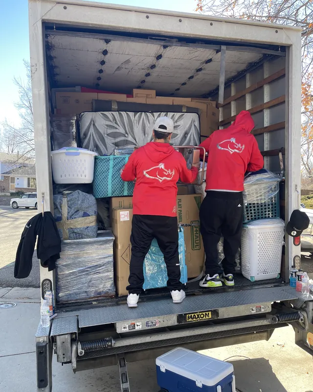 Two movers in red Rhino Brothers shirts beside a loaded moving truck